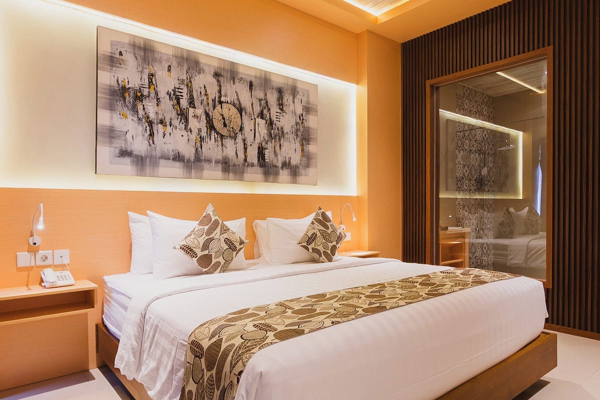 A modern bedroom with a large bed, a bedside table, a wall-mounted artwork, and a large mirror.