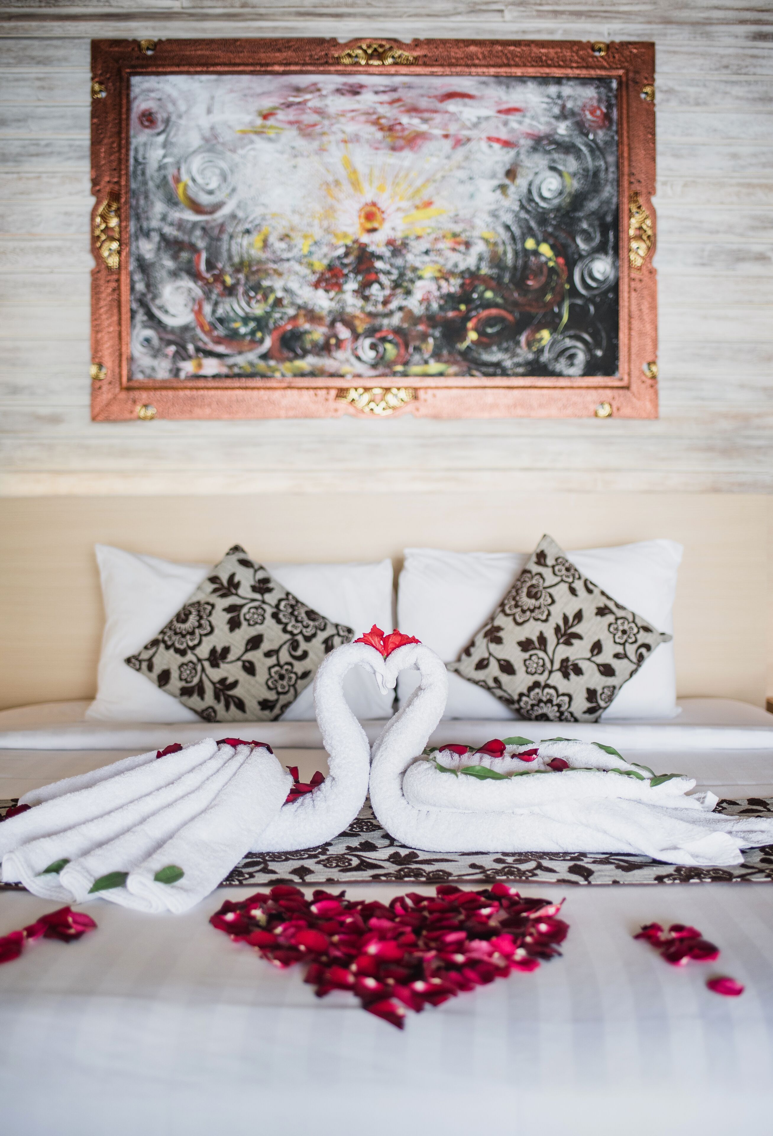 A bed with white linens, two swan-shaped towels, and rose petals.