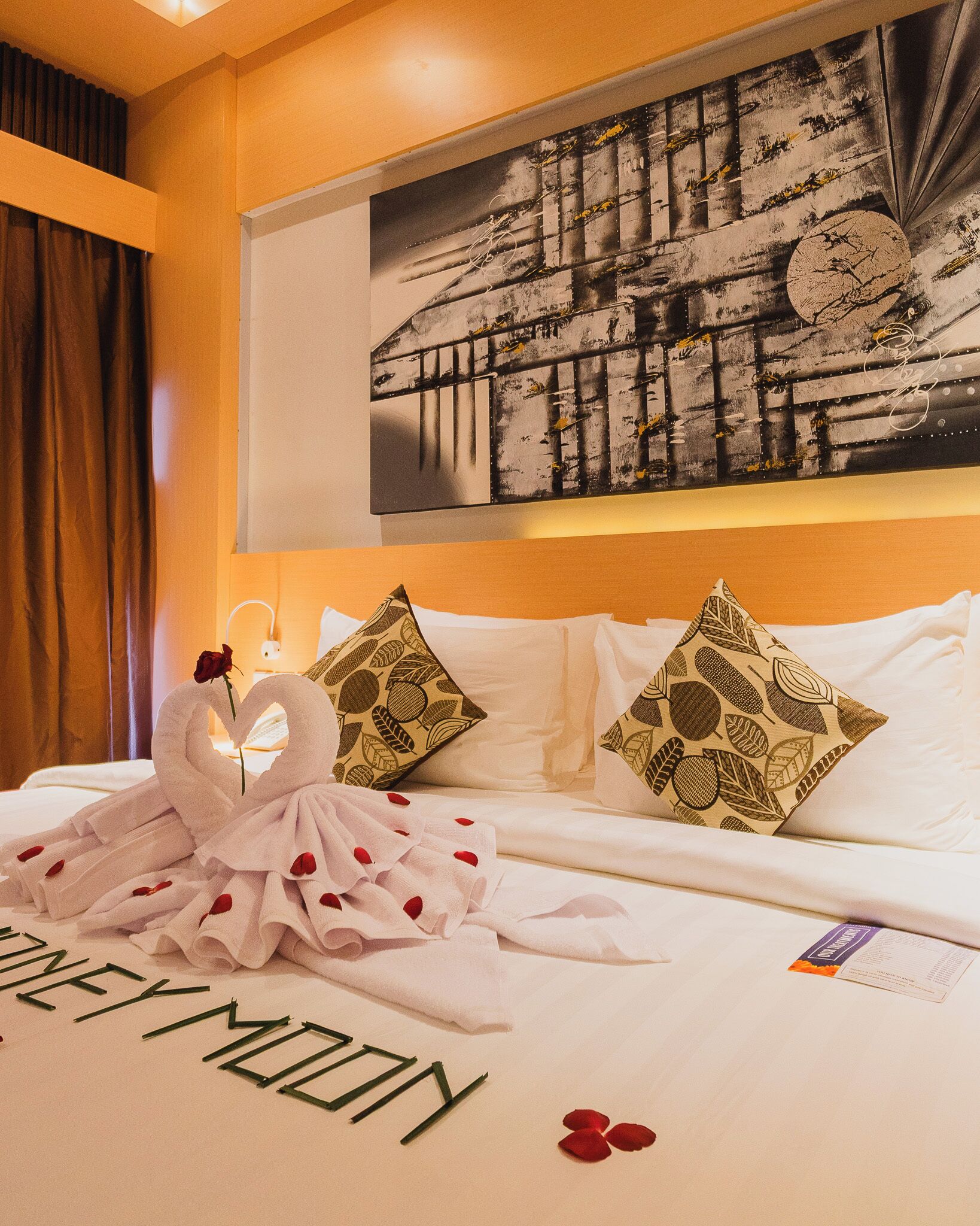A hotel room with a bed, a painting on the wall, and a bouquet of roses.