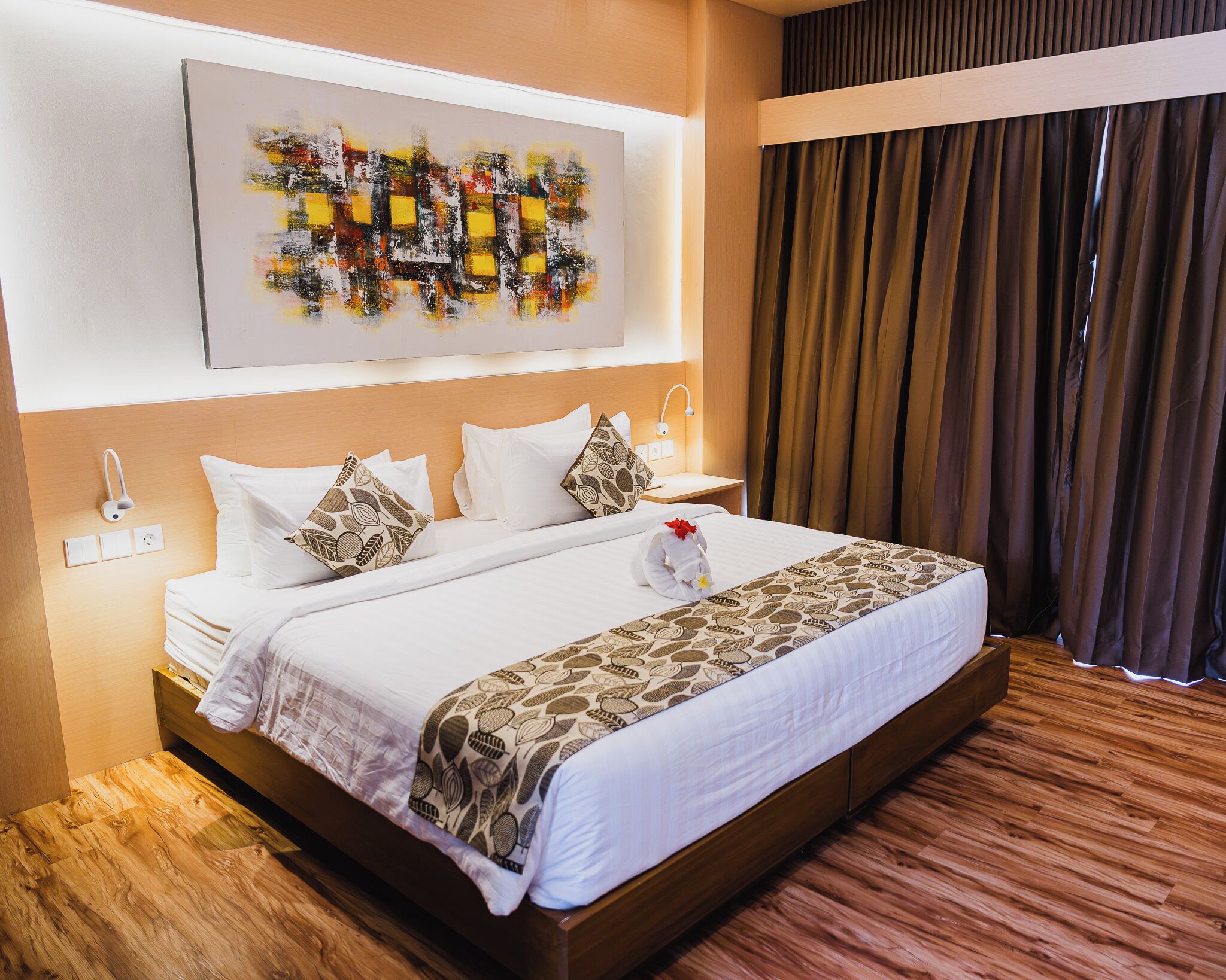 Una habitación de hotel con una cama grande, un cabecero, una mesita de noche, una obra de arte colgada en la pared y una ventana con cortinas.