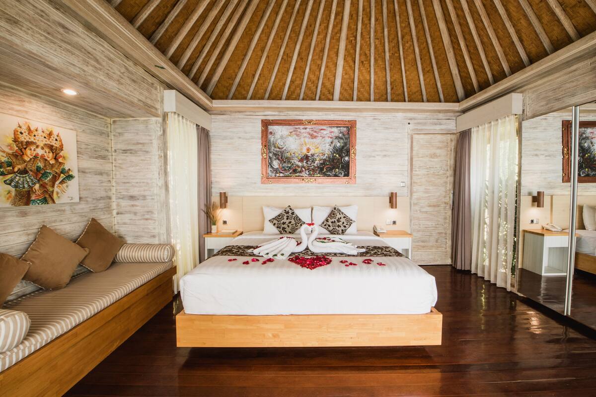A spacious bedroom with a large bed, wooden ceiling, and a painting above the bed.