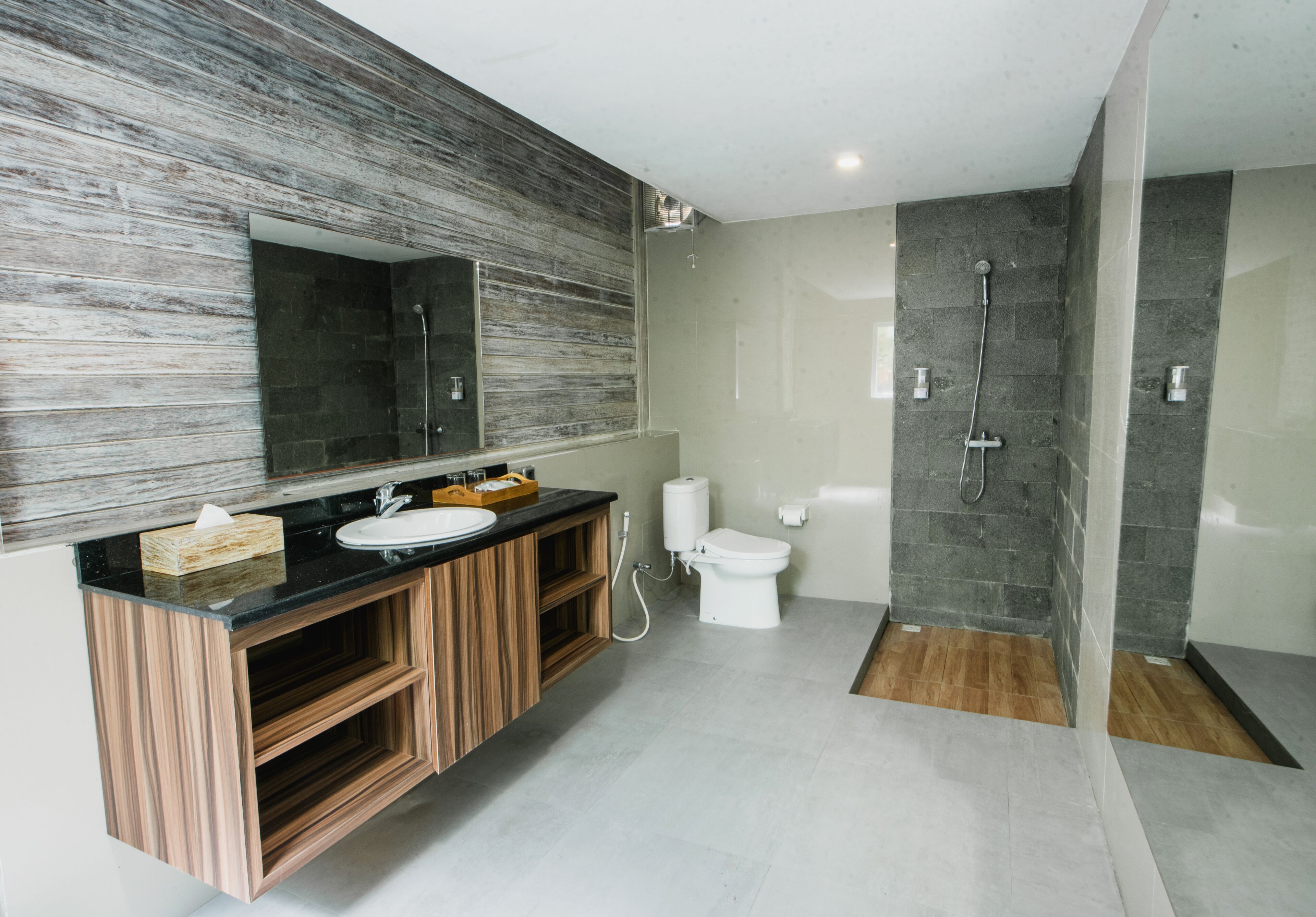 A modern bathroom with a wooden vanity, a large mirror, a white sink, and a separate toilet area.