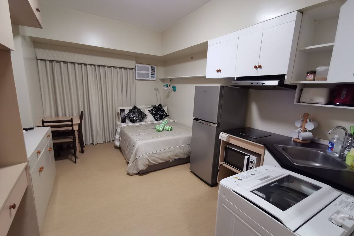 Kompakti hotellihuone, jossa on sänky, pieni keittokomero, pesukone ja ruokailutila.
