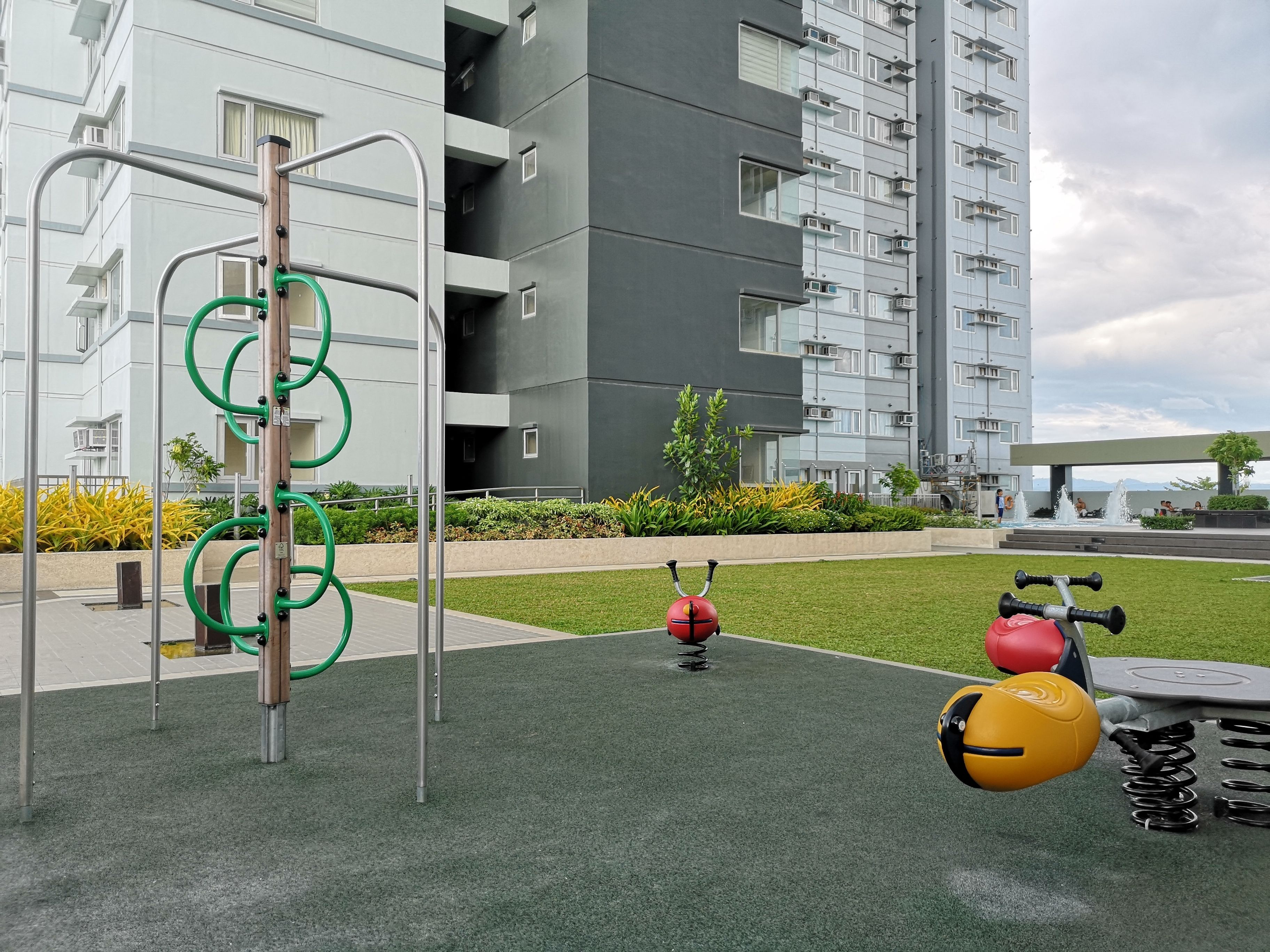 An outdoor gym area with exercise equipment, surrounded by a building with multiple balconies and a landscaped garden.