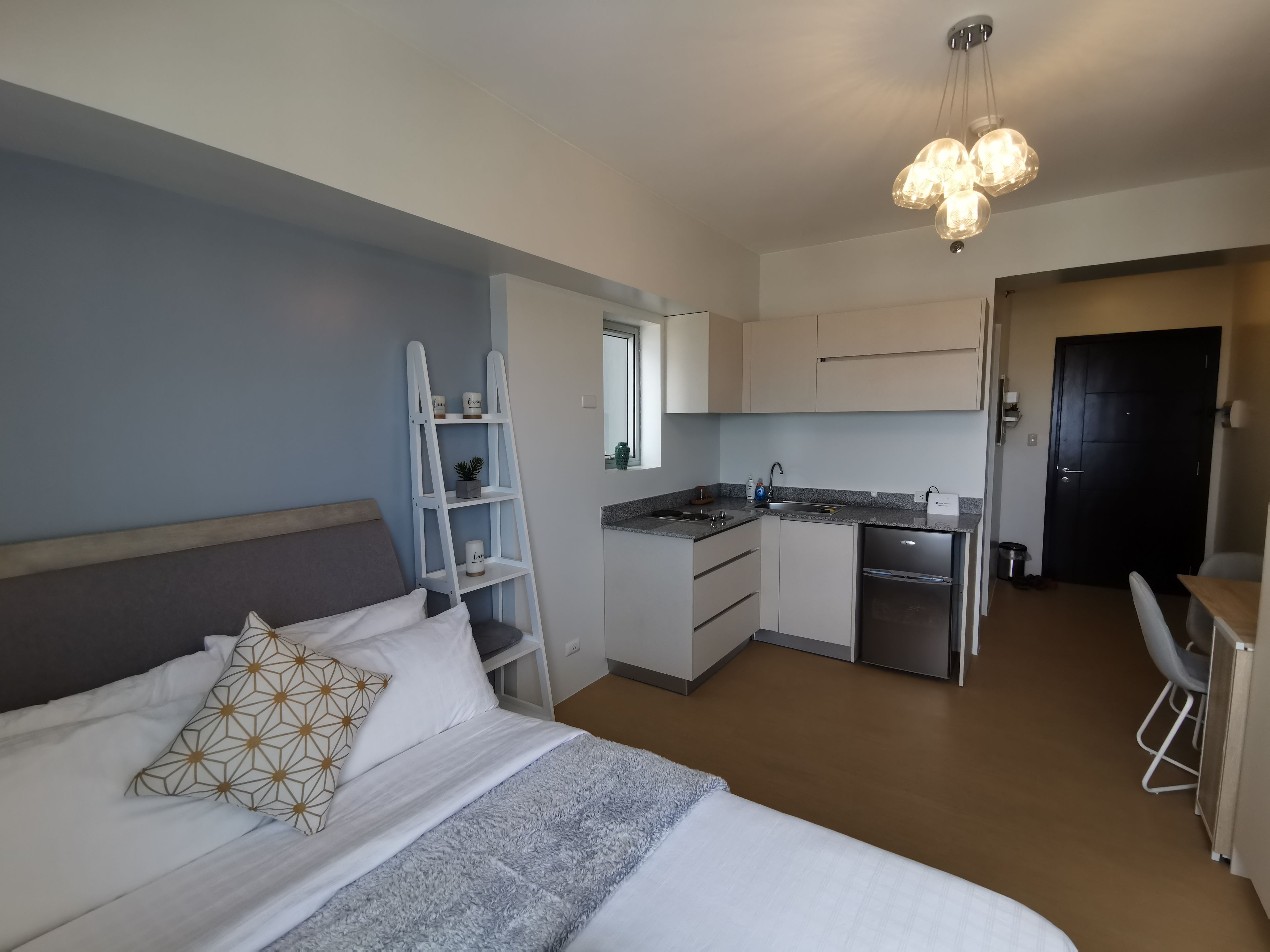 A compact room with a bed, a small kitchenette, and a desk.