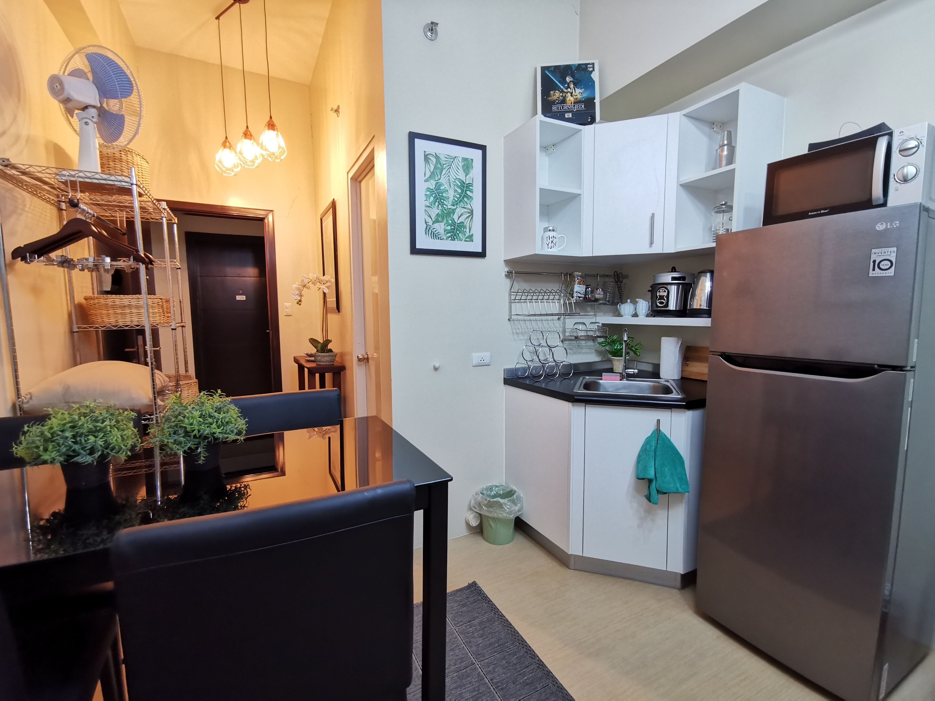 A modern kitchen with white cabinets, a stainless steel refrigerator, and a dining area with a black table and chairs.