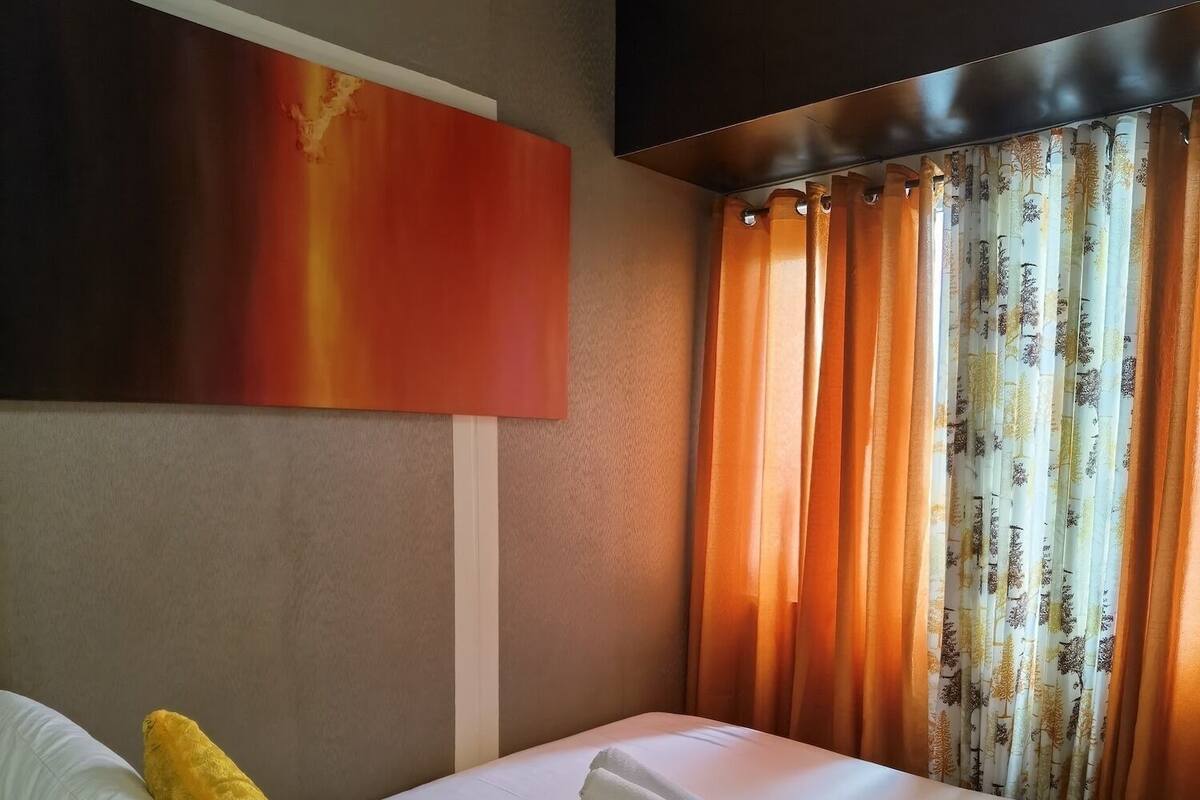 Hotellihuone, jossa on sänky, suuri taulu seinällä ja puukuviolliset verhot.
