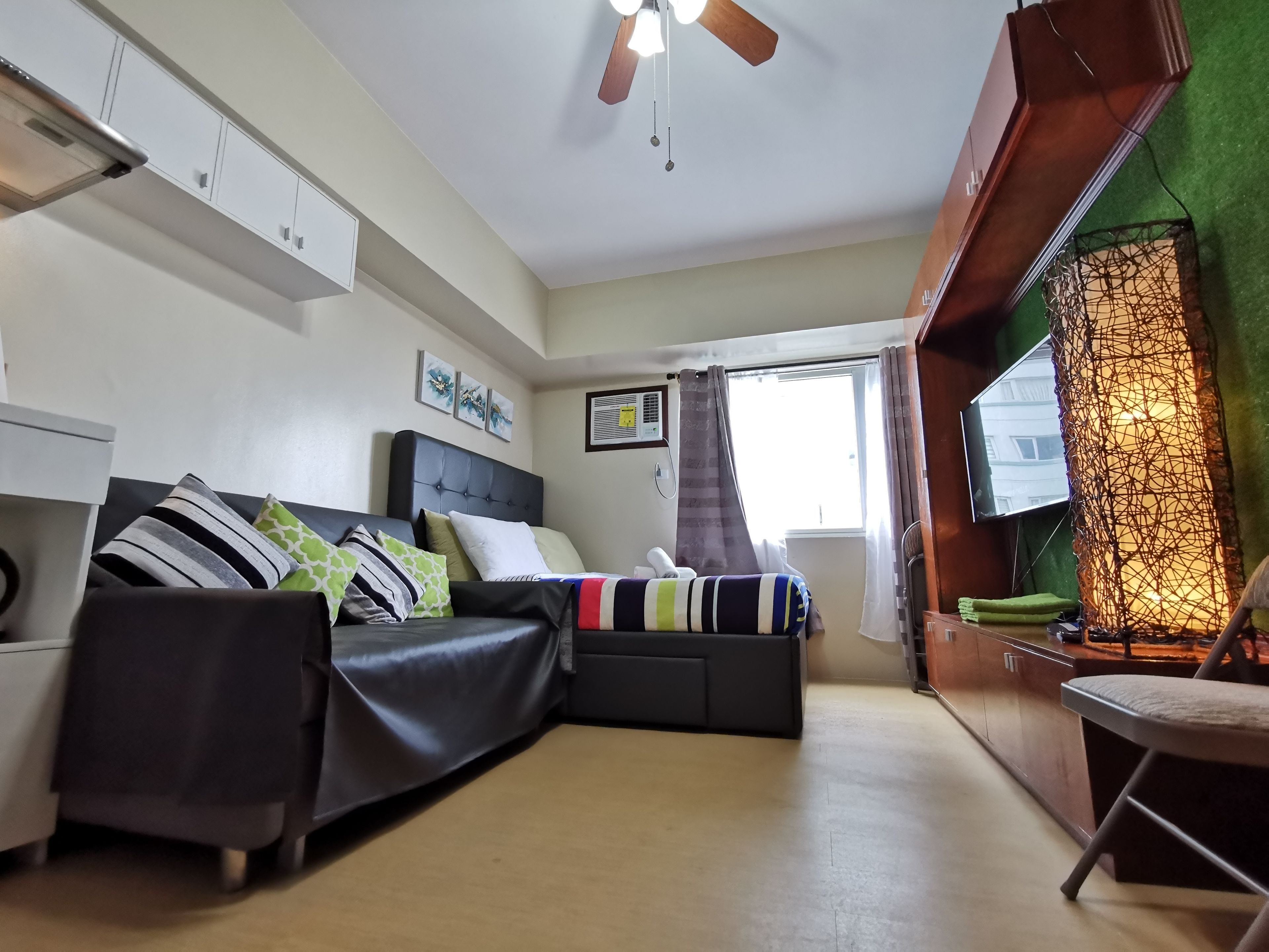 A compact bedroom with a bed, a ceiling fan, a window with curtains, and a TV mounted on the wall.