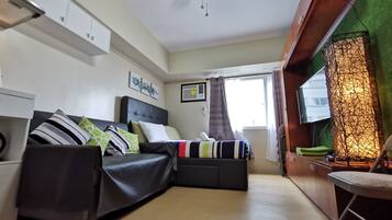A compact bedroom with a bed, a ceiling fan, a window with curtains, and a TV mounted on the wall.