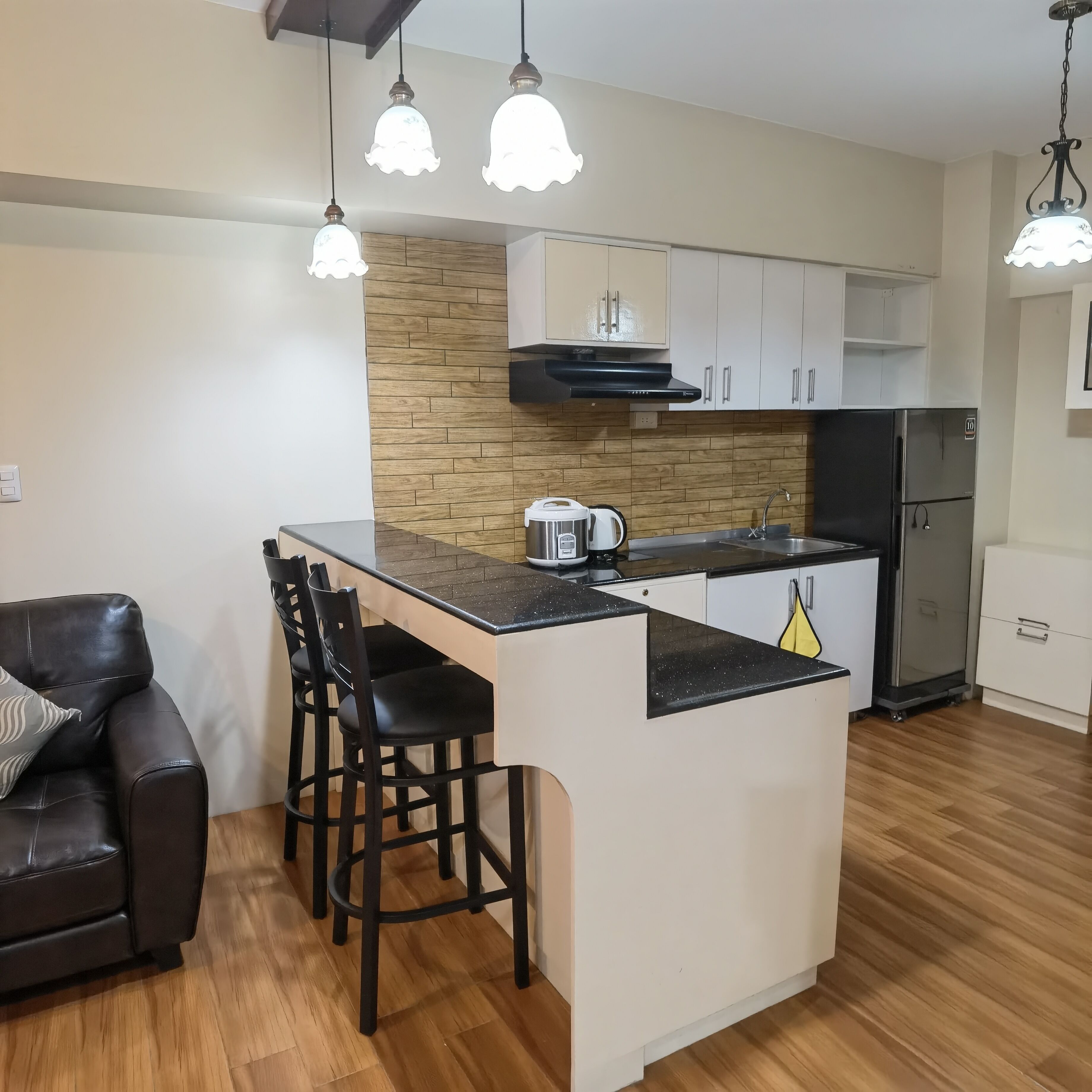 A modern kitchen with a central island, wooden flooring, and pendant lighting.