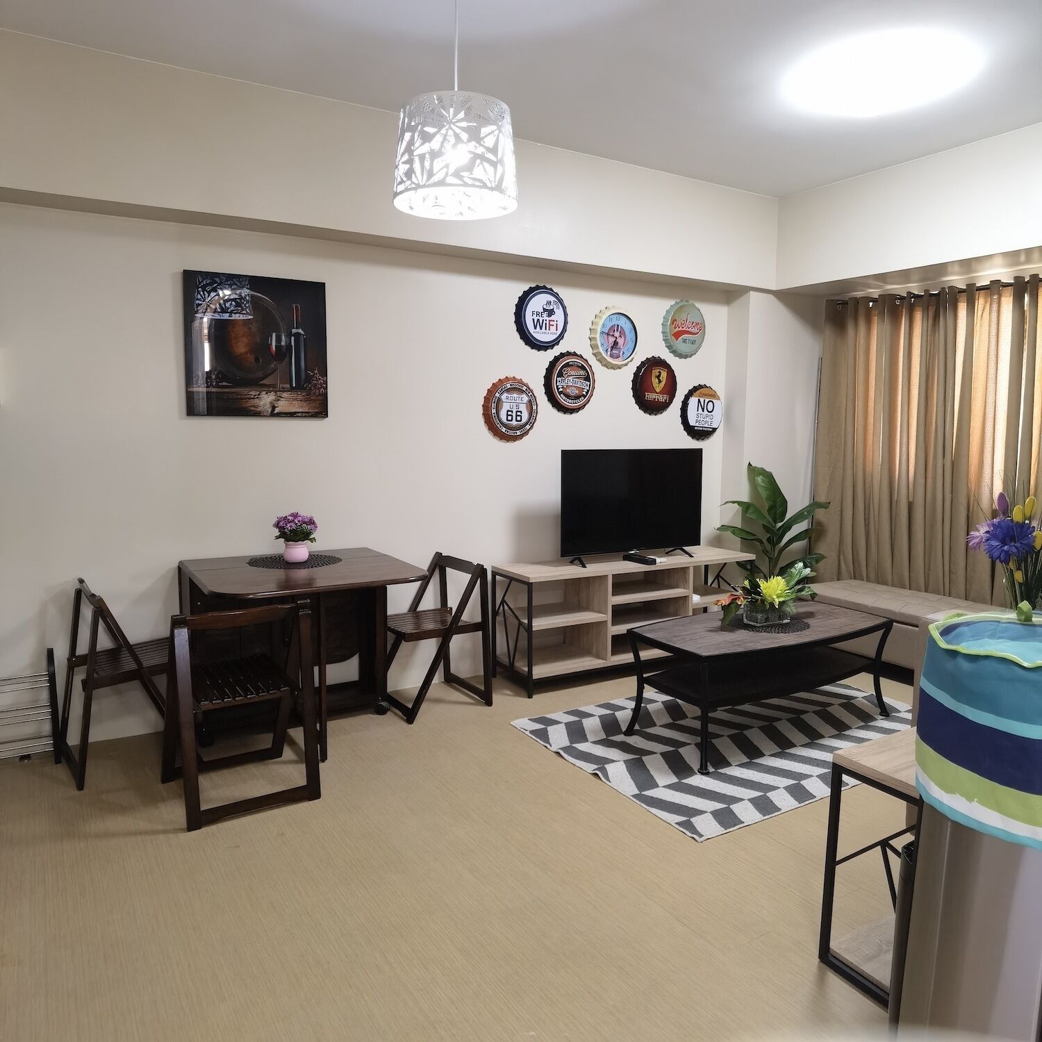 Un salon comprenant une table à manger, des chaises, une table basse, un téléviseur, des éléments décoratifs muraux et une grande fenêtre avec des rideaux.