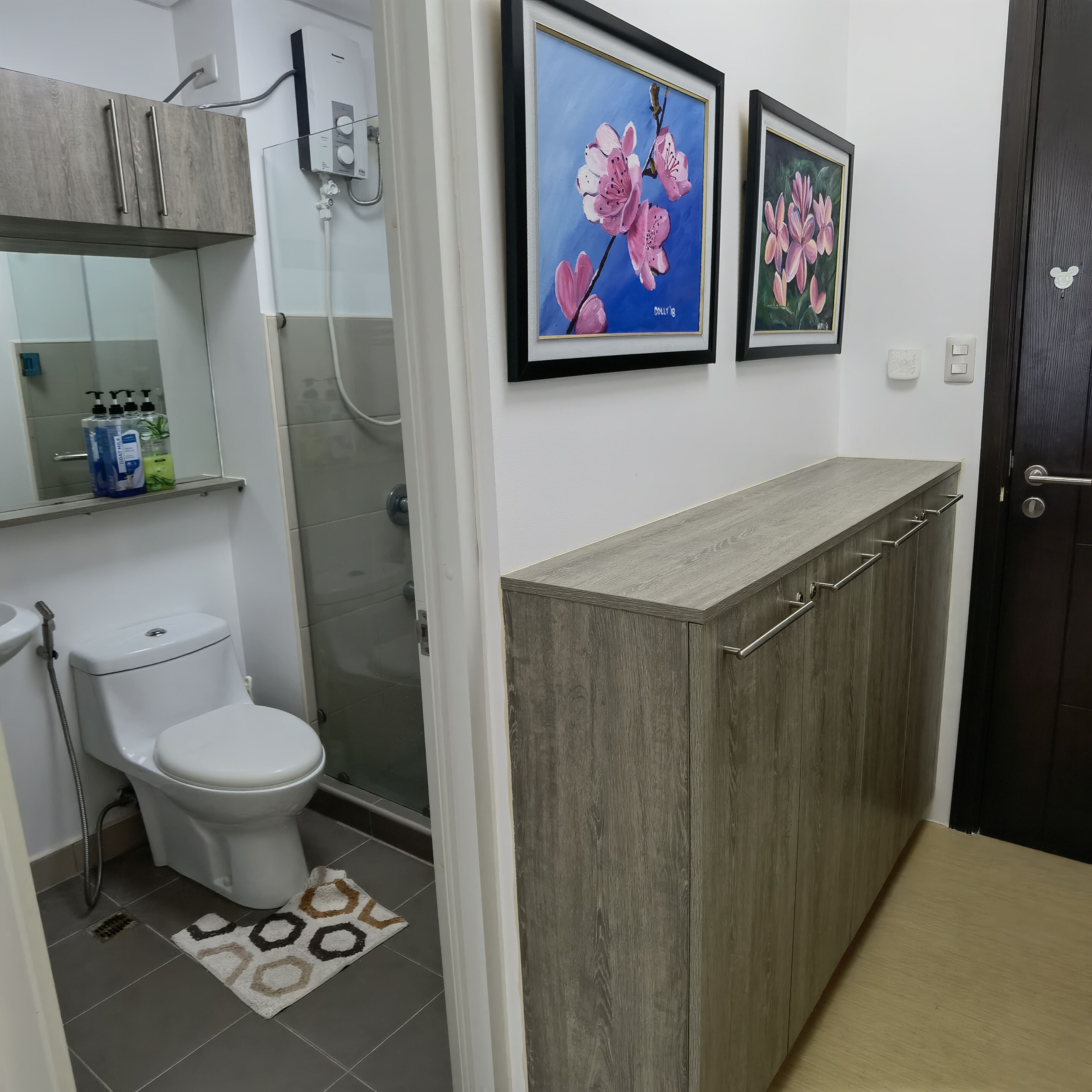 A bathroom with a toilet, shower, and a vanity with a mirror. There are two framed floral paintings on the wall.