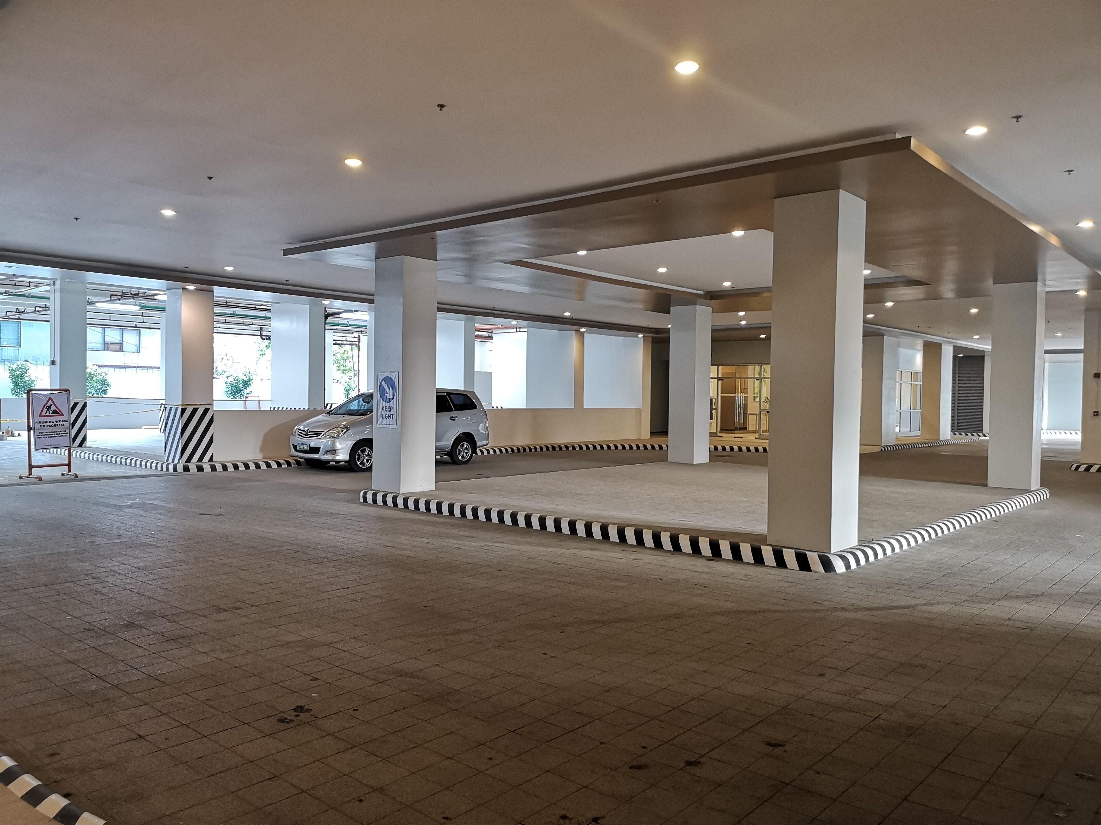 A spacious indoor parking area with a white car parked near a sign indicating construction work.