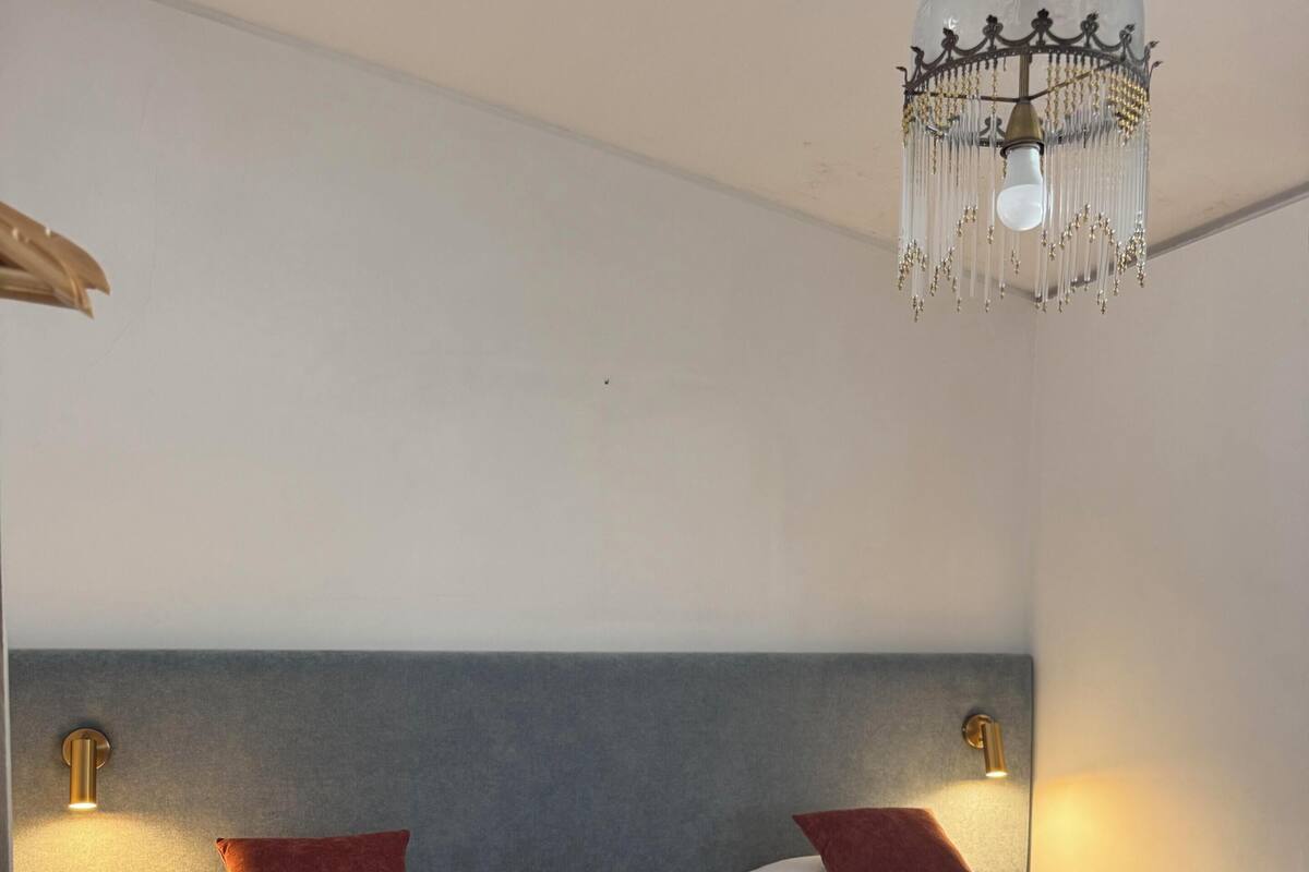 Habitación de hotel con dos camas, una araña, luces fijadas a la pared y suelo de madera.