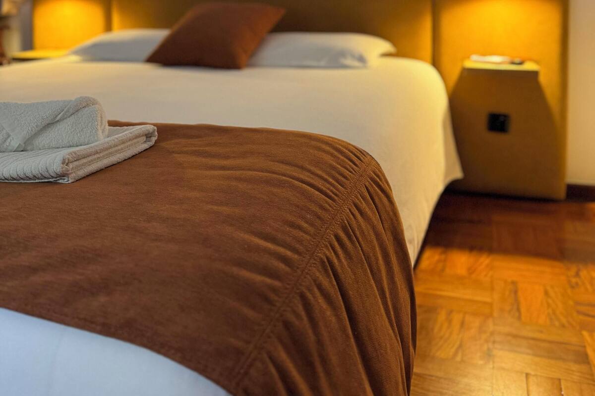 Una habitación de hotel con una cama grande, dos mesitas de noche y un aplique de pared.