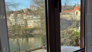 Une vue à travers la fenêtre d’un immeuble donnant sur une rivière, avec d’autres immeubles et un pont en arrière-plan.
