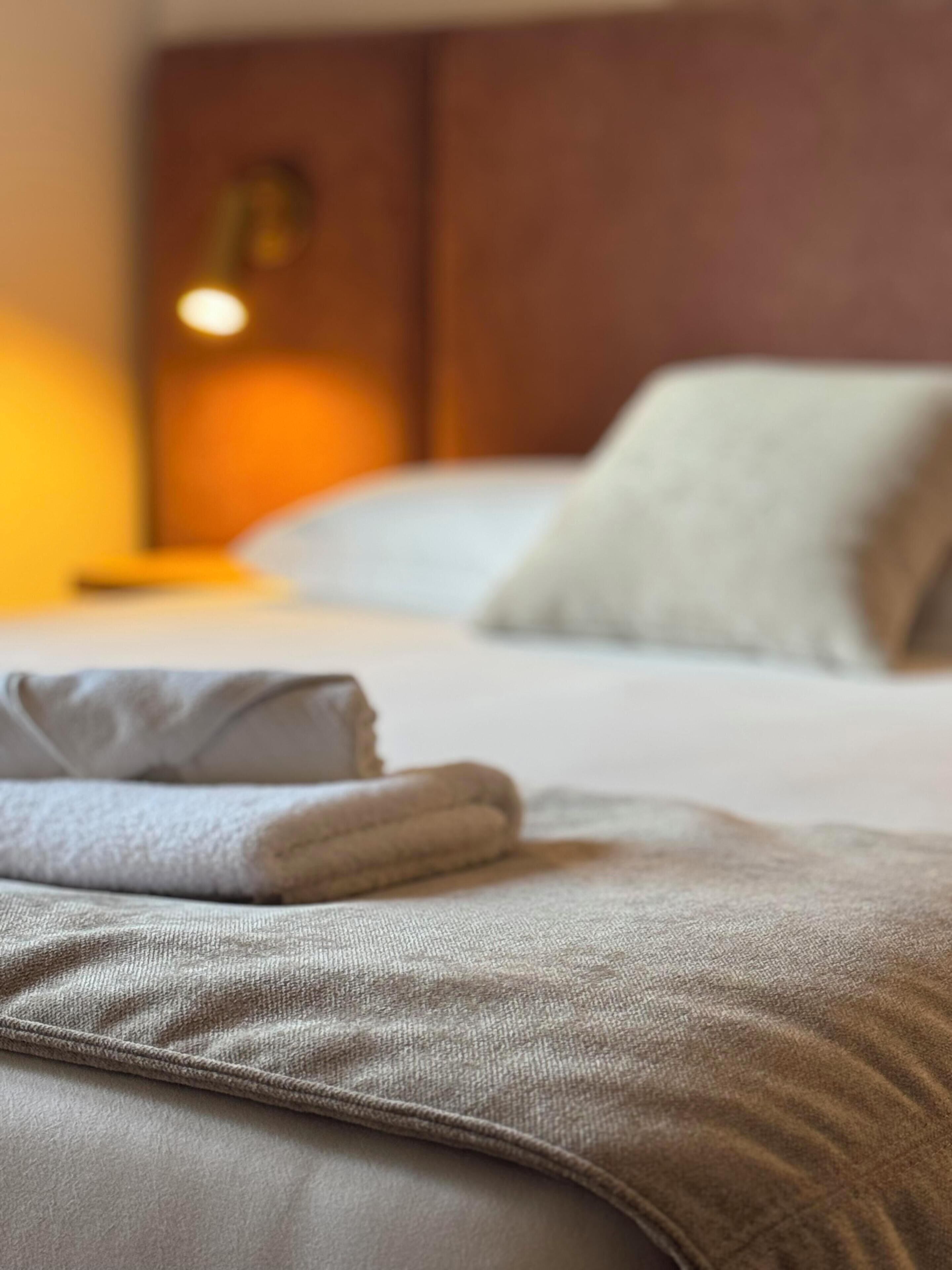 Un lit bien fait, avec un oreiller et une couverture pliée, dans une chambre d’hôtel.