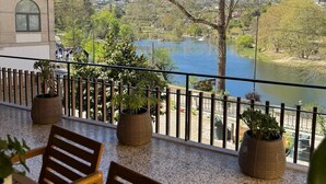 Un balcon agrémenté de chaises en bois et de plantes en pot, d’où l’on peut admirer un lac et un paysage vallonné.