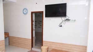 Hotellihuone, jossa on puulattia, seinälle asennettu televisio, puinen kaappi, roskakori ja ovi, joka johtaa toiseen huoneeseen.