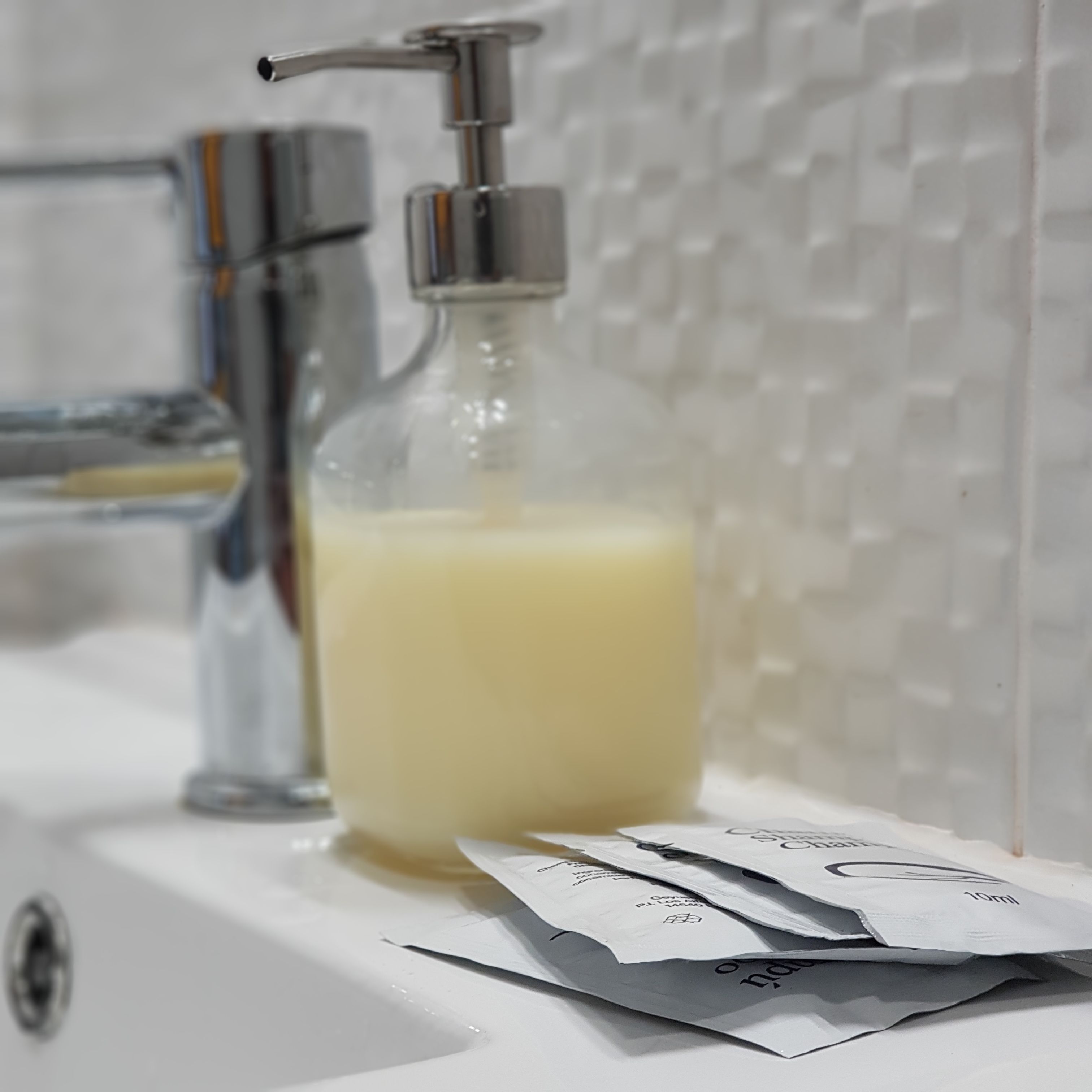 Une salle de bain avec un distributeur de savon en verre et un lavabo.