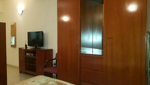 Ein Zimmer mit einem Holzkleiderschrank, einem Fernseher auf einer Holzkommode und einem Sessel.