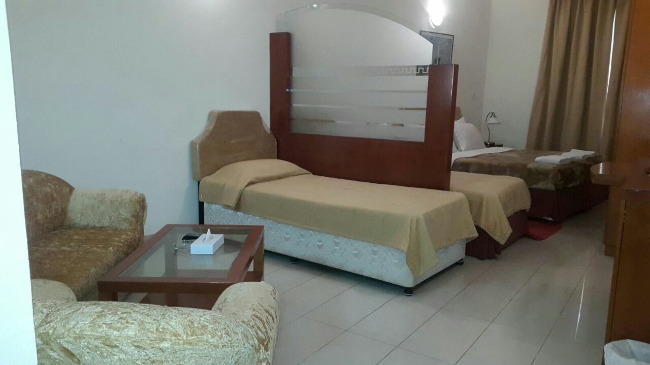 A hotel room with a bed, two bedside tables, a sofa, and a small table with a remote control.