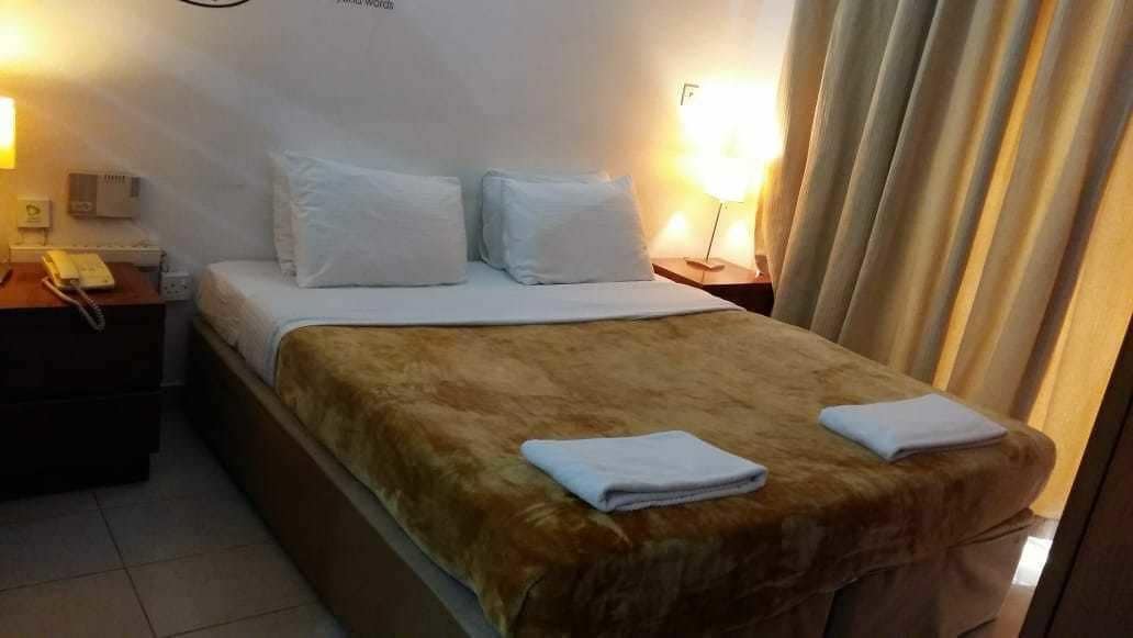 A hotel room with a bed, a bedside table with a lamp, a phone, and a curtain.