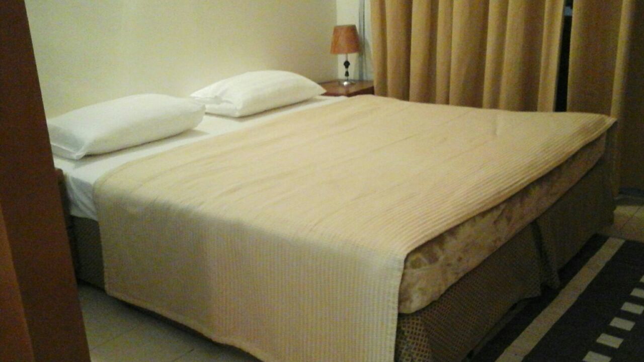 A hotel room with a bed, a nightstand with a lamp, and a window with curtains.