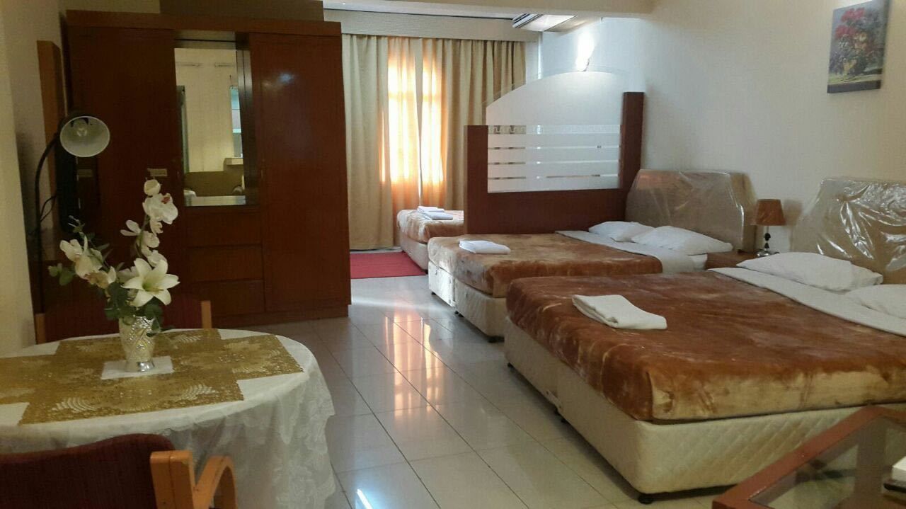 A hotel room with two beds, a dining table with a vase of flowers, and a mirror.