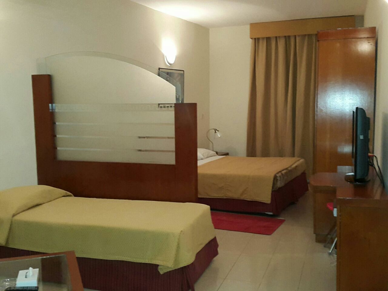 Camera d'albergo con due letti singoli, una scrivania, una sedia, una televisione e uno specchio.