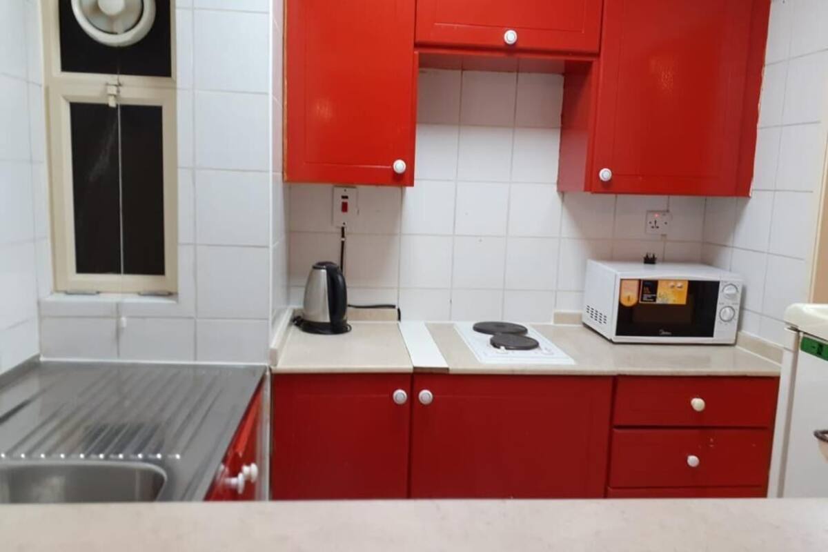 Eine Küche mit roten Schränken, einer Mikrowelle, einem Wasserkocher und einem Fenster mit Jalousien.
