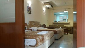 Ein Hotelzimmer mit zwei Betten, einem Schlafsofa, einem kleinen Tisch und einer Küchenzeile im Hintergrund.