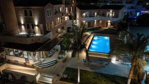 Un hôtel à plusieurs étages doté d’une piscine, d’un espace extérieur aménagé et d’une entrée bien éclairée.