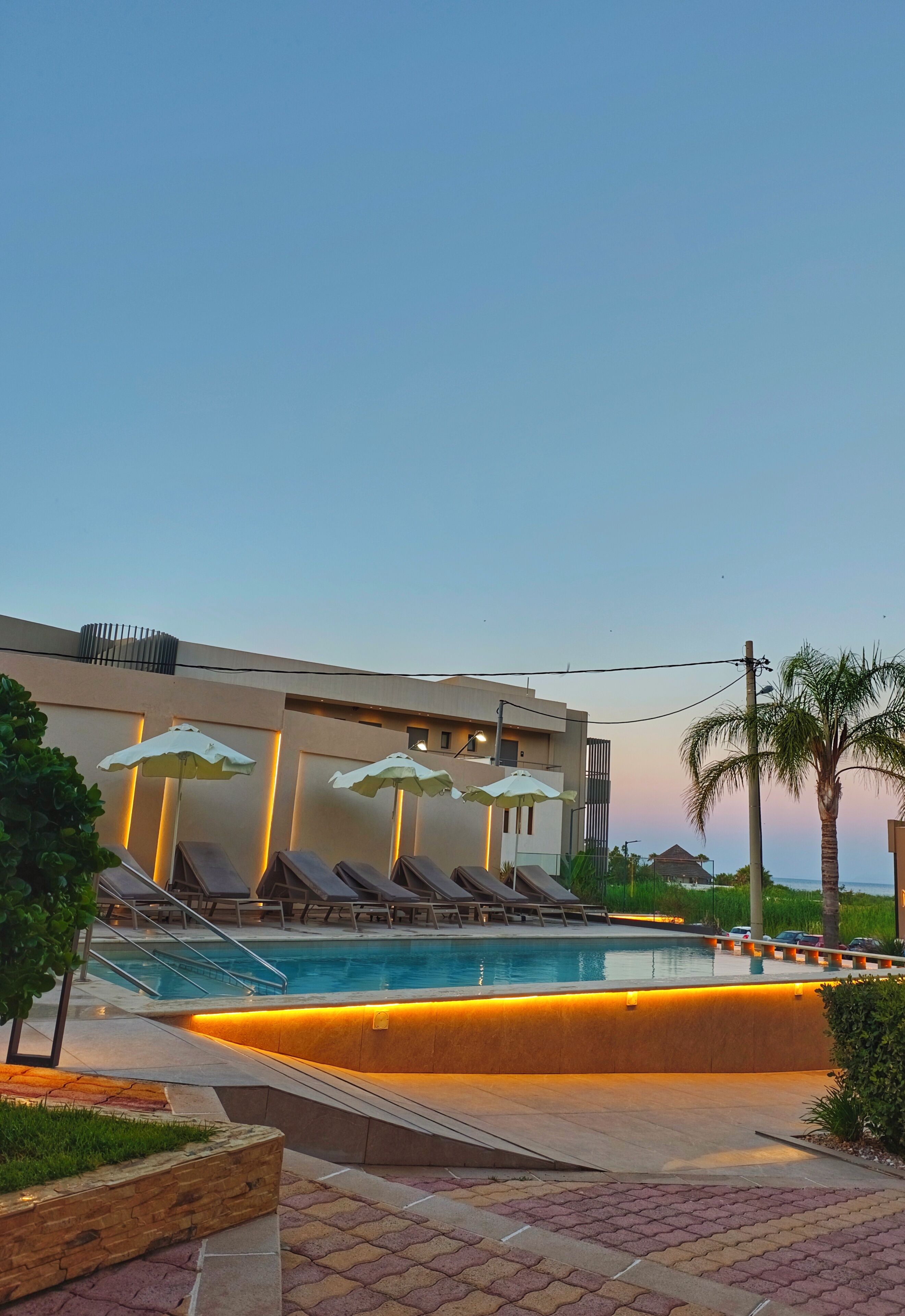 A swimming pool with sun loungers, umbrellas, and a building with a modern design.