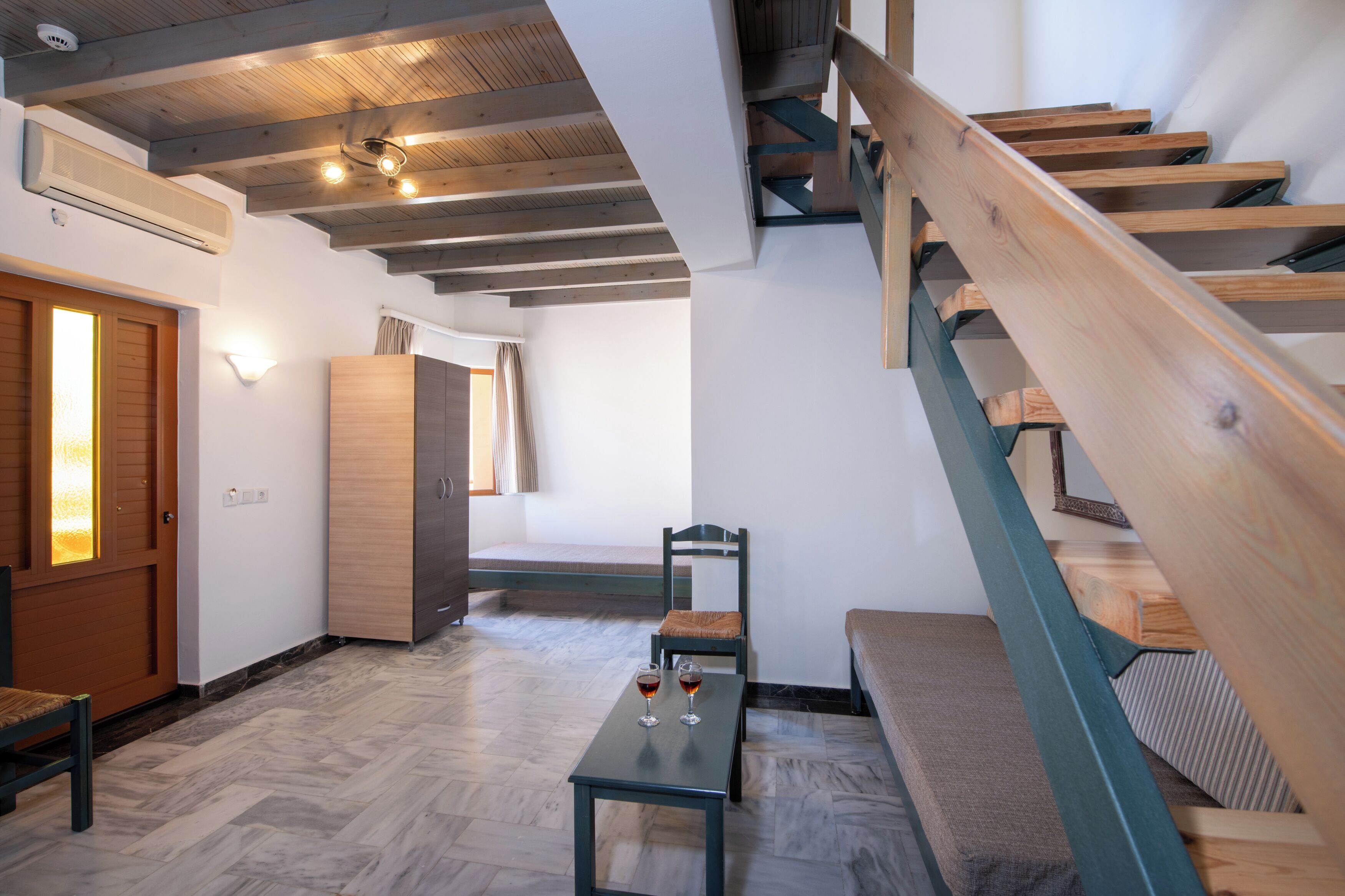 A modern interior with a wooden staircase, a bench, a table with glasses, and a bed.