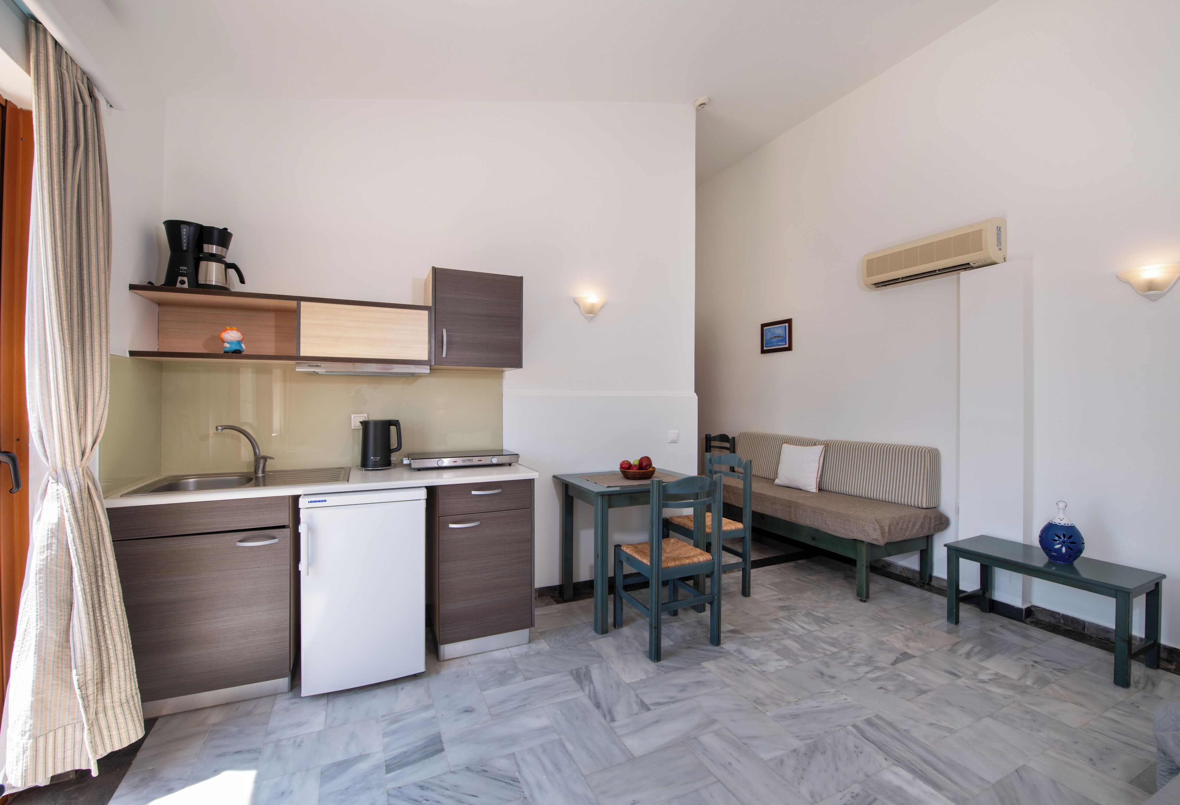 A compact kitchen with a sink, coffee maker, and a small refrigerator. There is a dining area with a table and chairs, and a sofa.