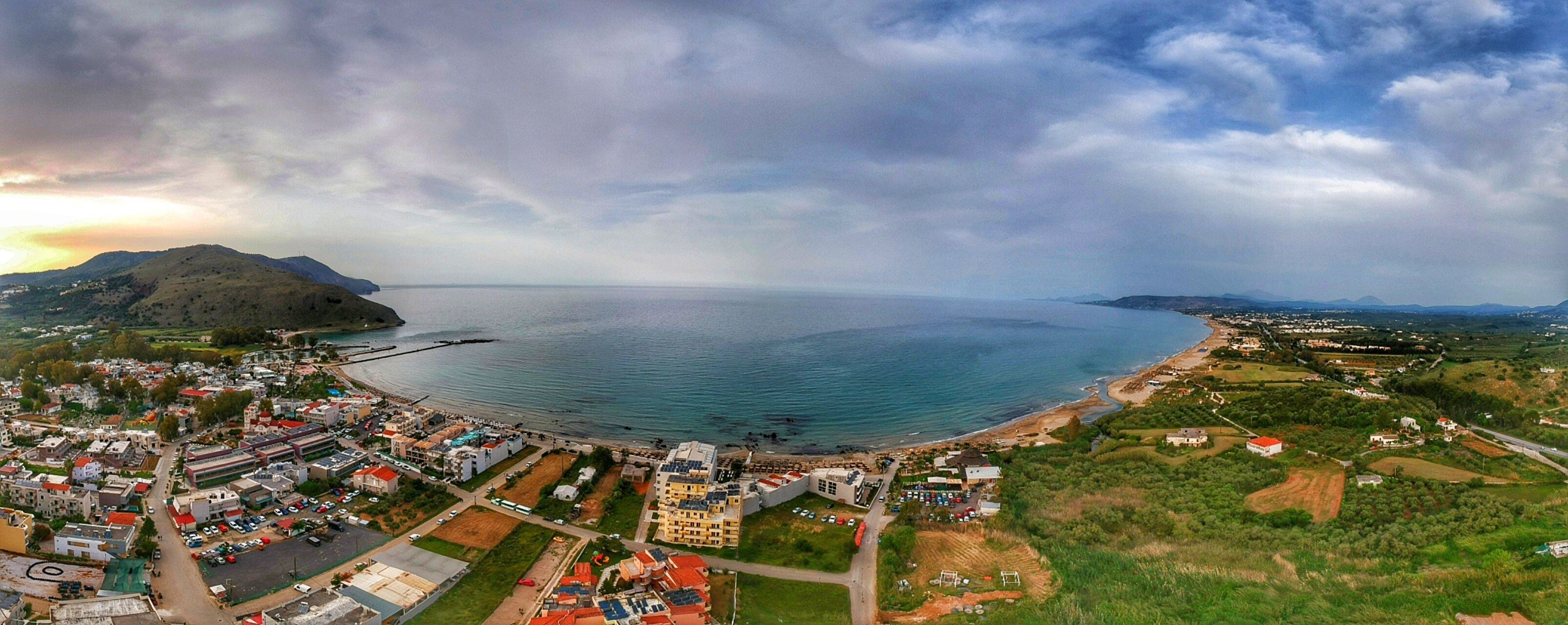 An aerial view of a coastal town with a beach, buildings, and a hilly landscape.