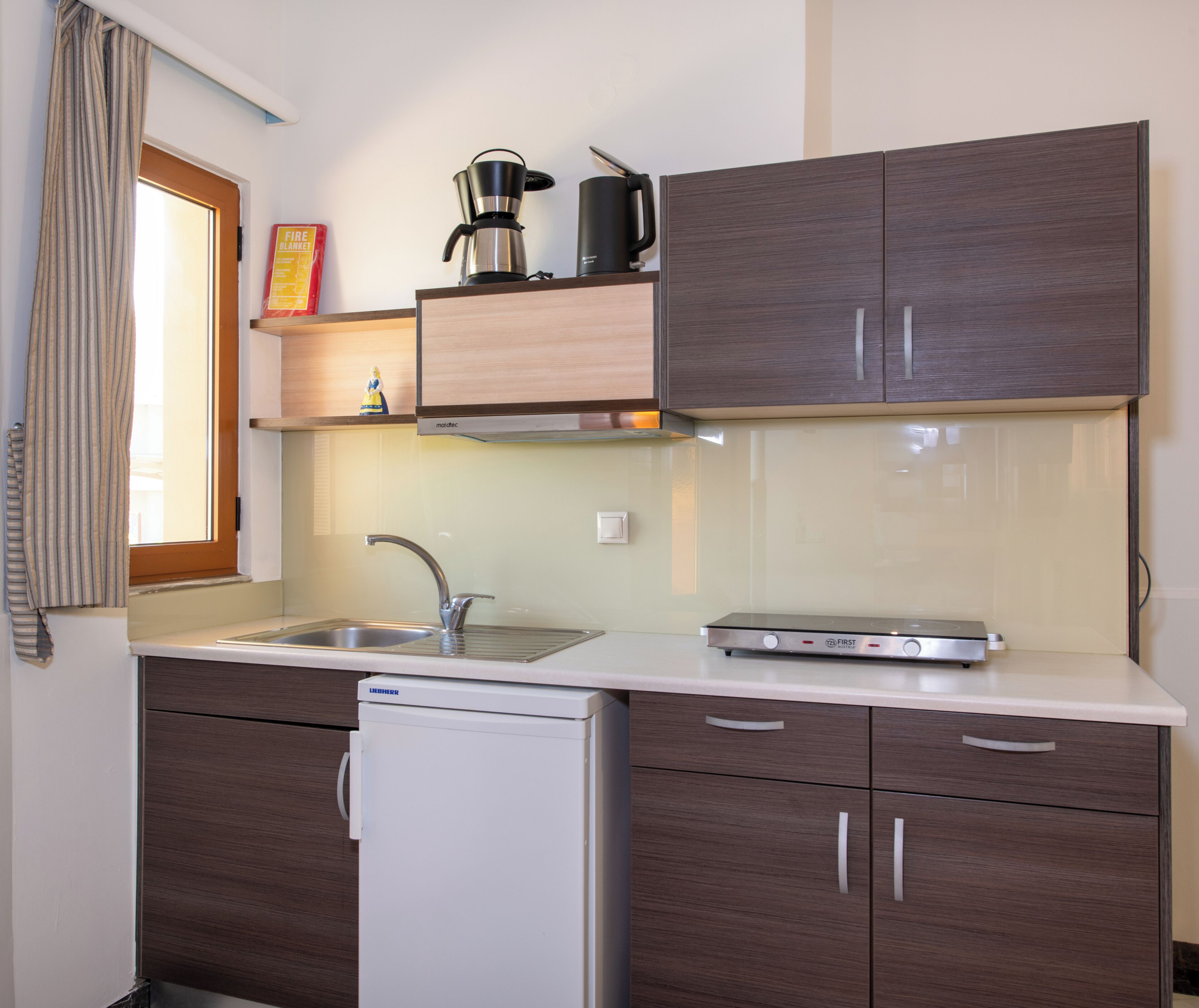 A compact kitchen with a sink, a coffee maker, and a compact dishwasher.