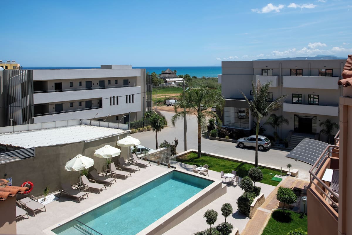 Un área de piscina en la azotea con sillones y sombrillas, una piscina y vistas al océano.