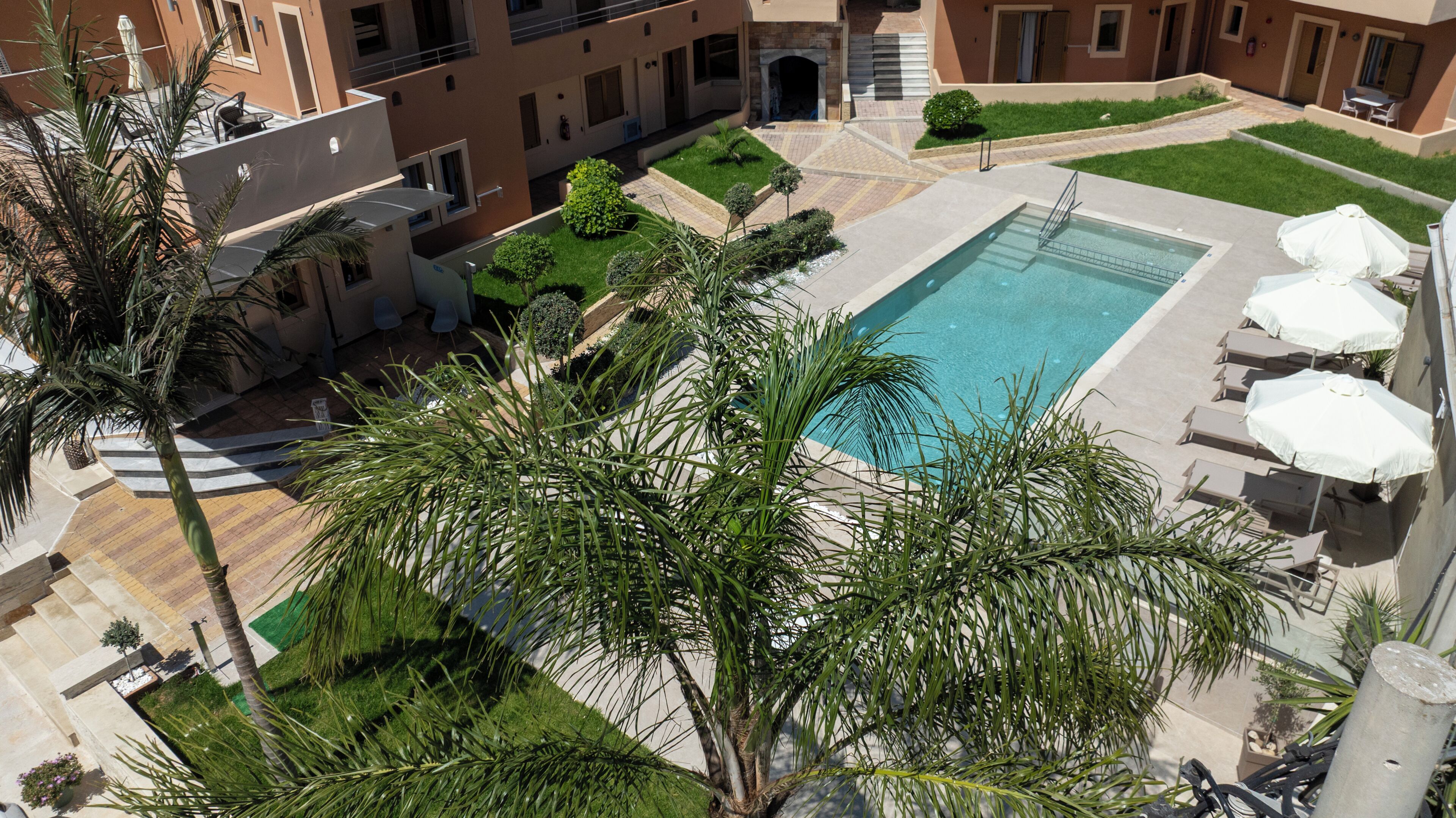 Une piscine sur le toit, agrémentée de chaises longues et de parasols, entourée de palmiers et bordée d’un immeuble doté de nombreux balcons.