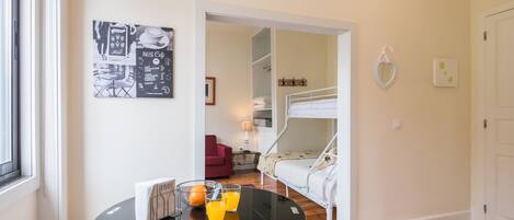 Une chambre avec un lit superposé, une table en verre sur laquelle se trouve un plateau avec du jus d’orange, et un menu encadré accroché au mur.