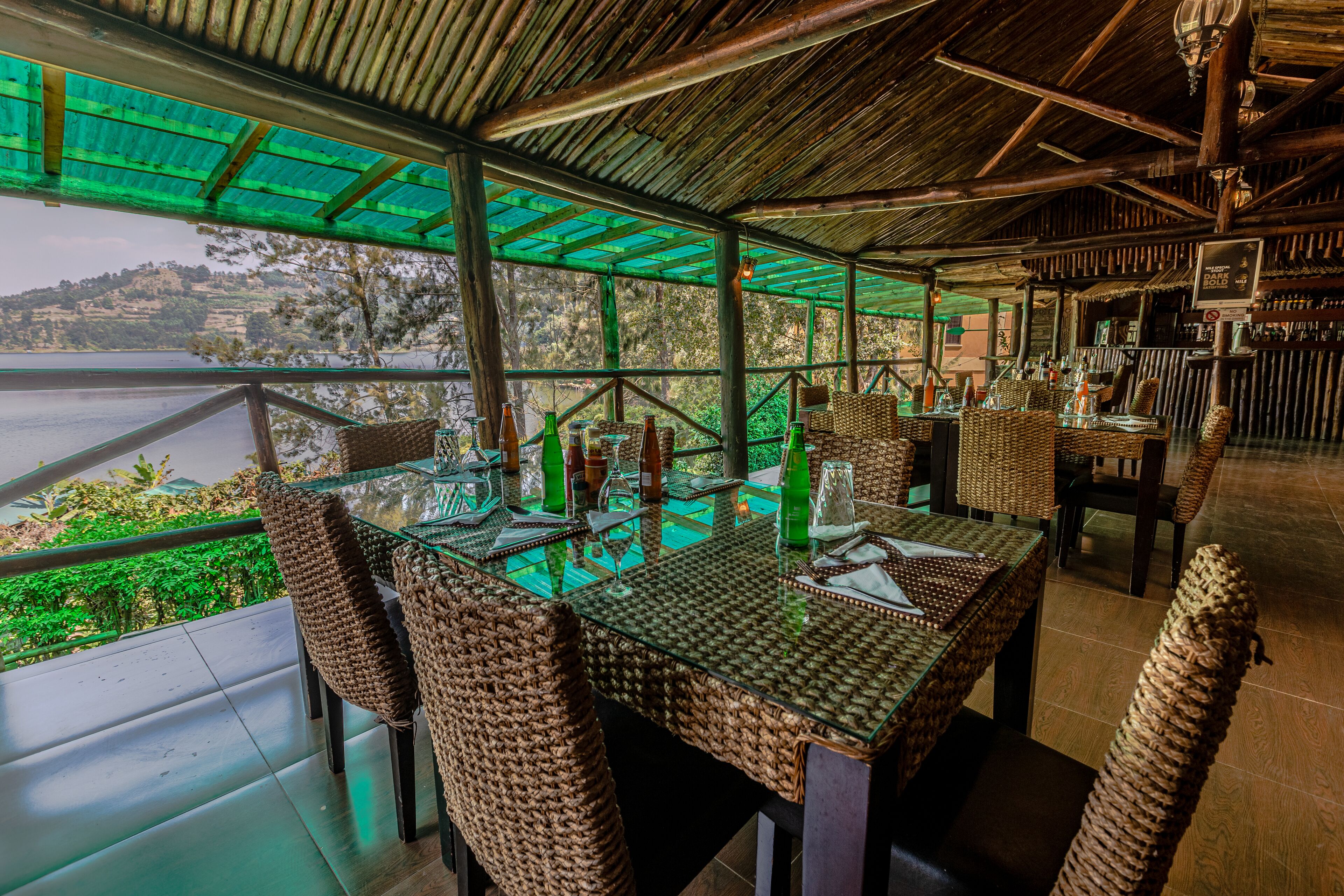 An outdoor dining area with wicker chairs and tables, overlooking a body of water and hills.
