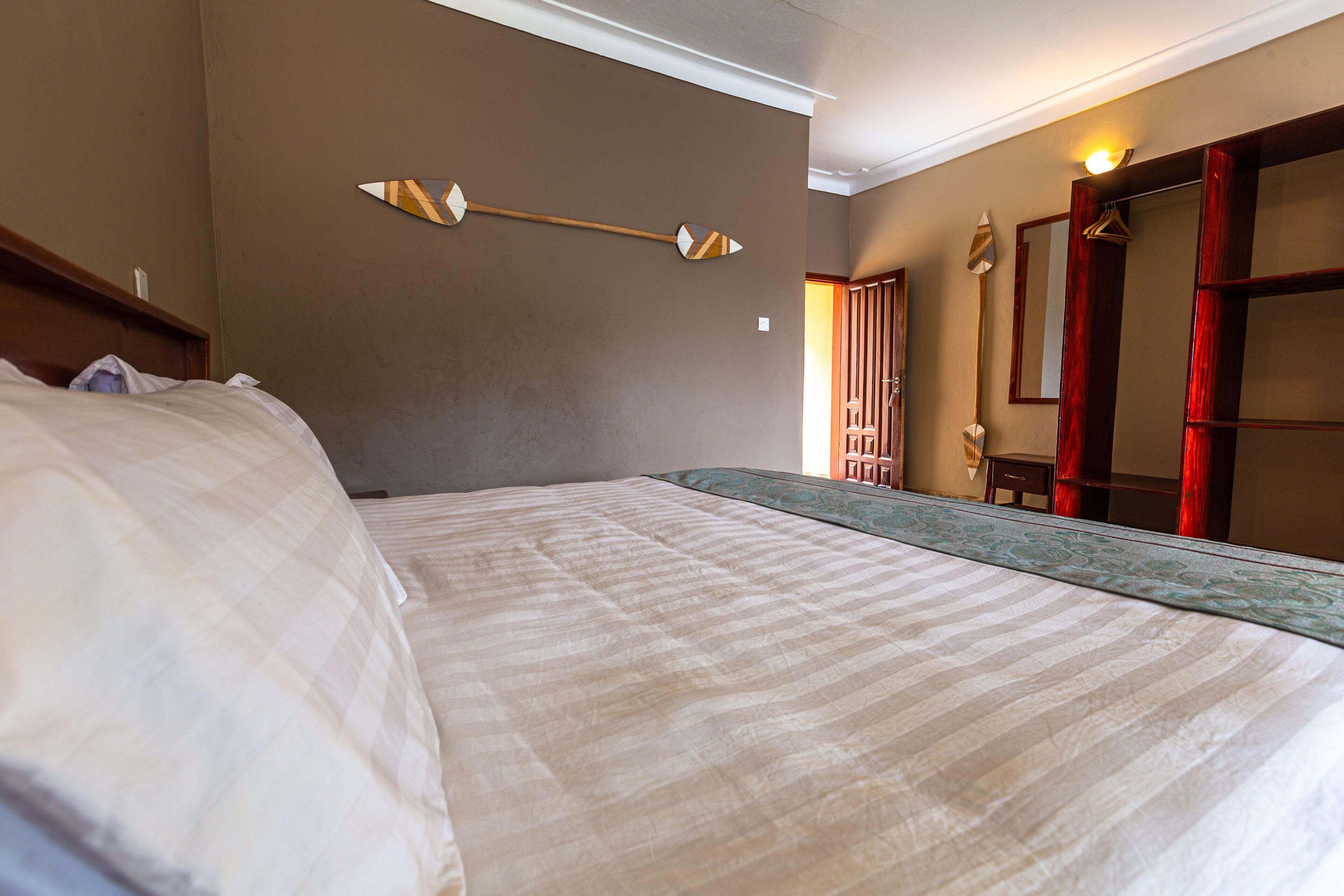 Una habitación de hotel con una cama grande, cabecera de madera, una lámpara fijada a la pared y un espejo con marco de madera.