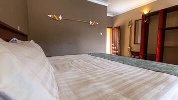 Una habitación de hotel con una cama grande, cabecera de madera, una lámpara fijada a la pared y un espejo con marco de madera.