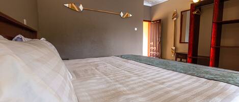 A hotel room with a large bed, a wooden headboard, a wall-mounted light fixture, and a mirror with a wooden frame.