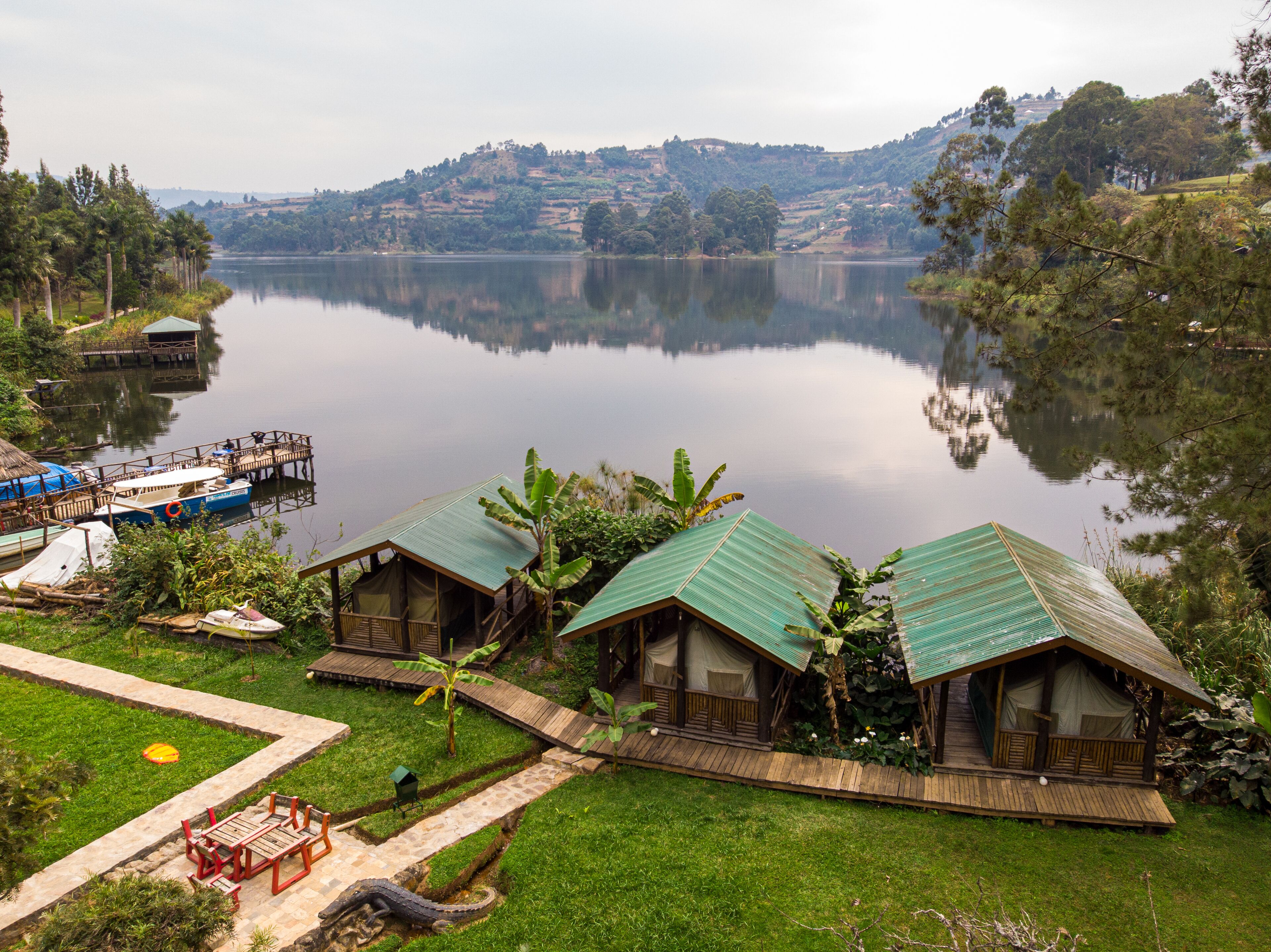 Acomodação à beira de um lago com duas cabanas de madeira, um cais com barcos e uma área gramada com um banco vermelho.