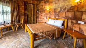 A rustic room with a stone floor, wooden bed, and a table with wine glasses. - Bunyonyi Overland Resort (Kabale)