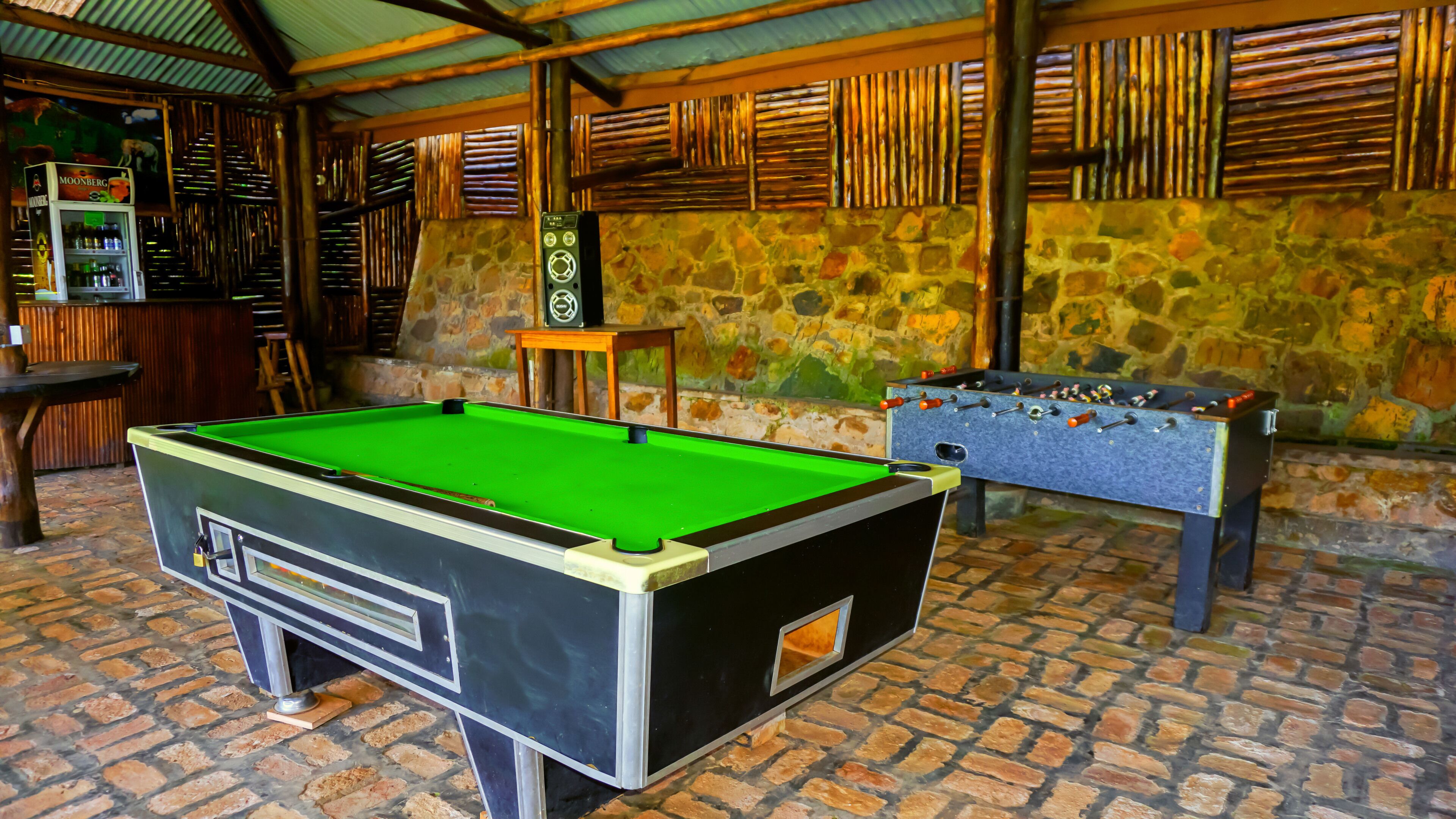 Una mesa de billar, una mesa de futbolín y una mesa de billar americano en una sala con paredes de piedra y techo de madera.