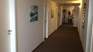 A hallway with white walls, brown carpet, and doors leading to rooms. There are framed pictures on the walls. - Sefano Seminarfabrik Nossen (Nossen)