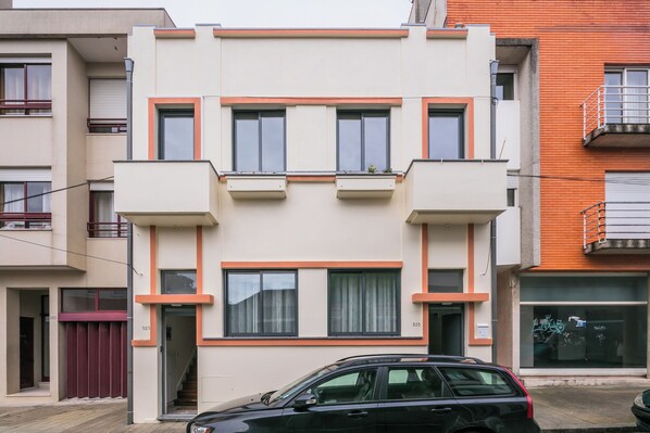 A modern two-story building with a flat roof, rectangular windows, and a balcony on the second floor.